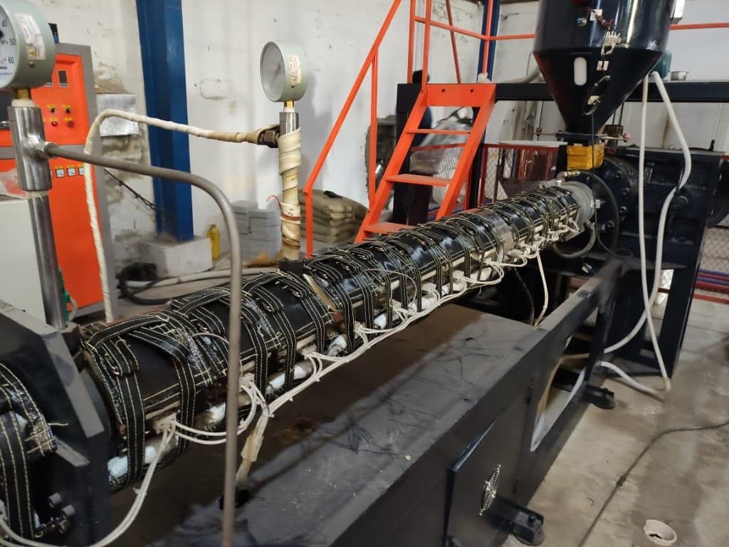 Industrial extruder barrel with heater zones and pressure gauges on a plant floor